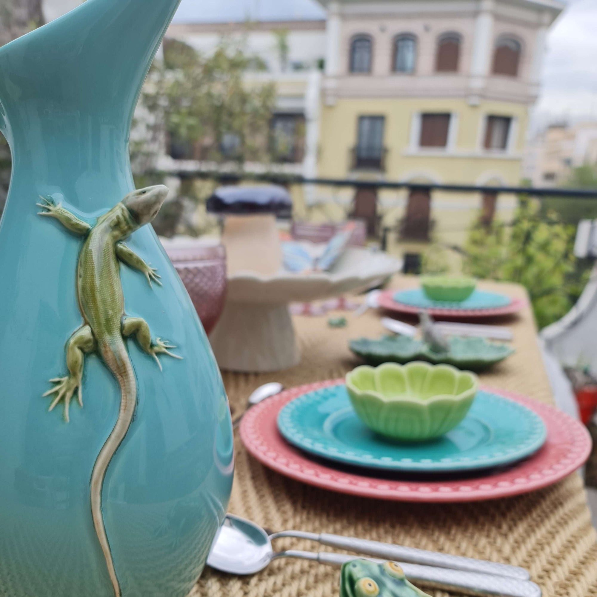 Bordallo Pitcher Vase with Lizard on a table with colorful plates and bowls outdoors.