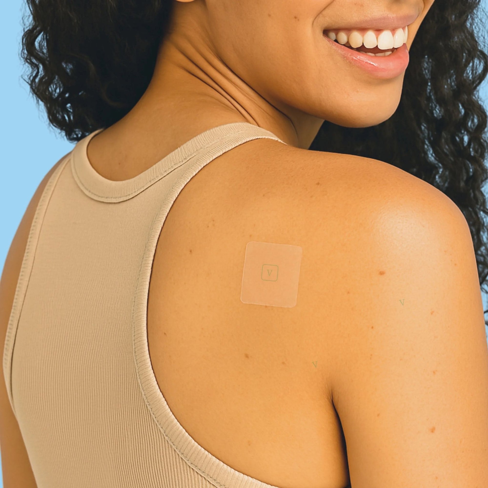Woman wearing a beige tank top with a patch on her shoulder against a blue background