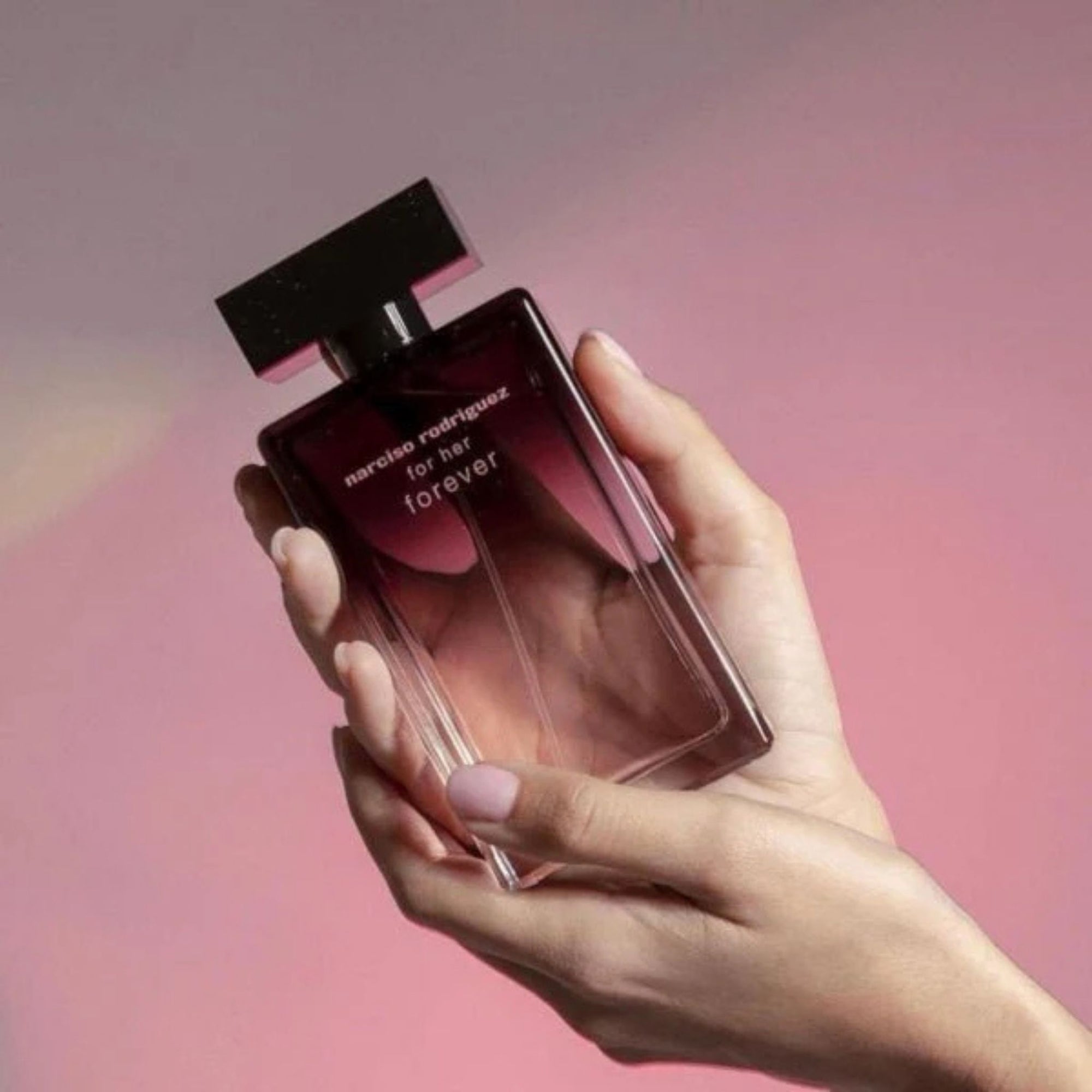 Hand holding a Narciso Rodriguez perfume bottle against a pink background
