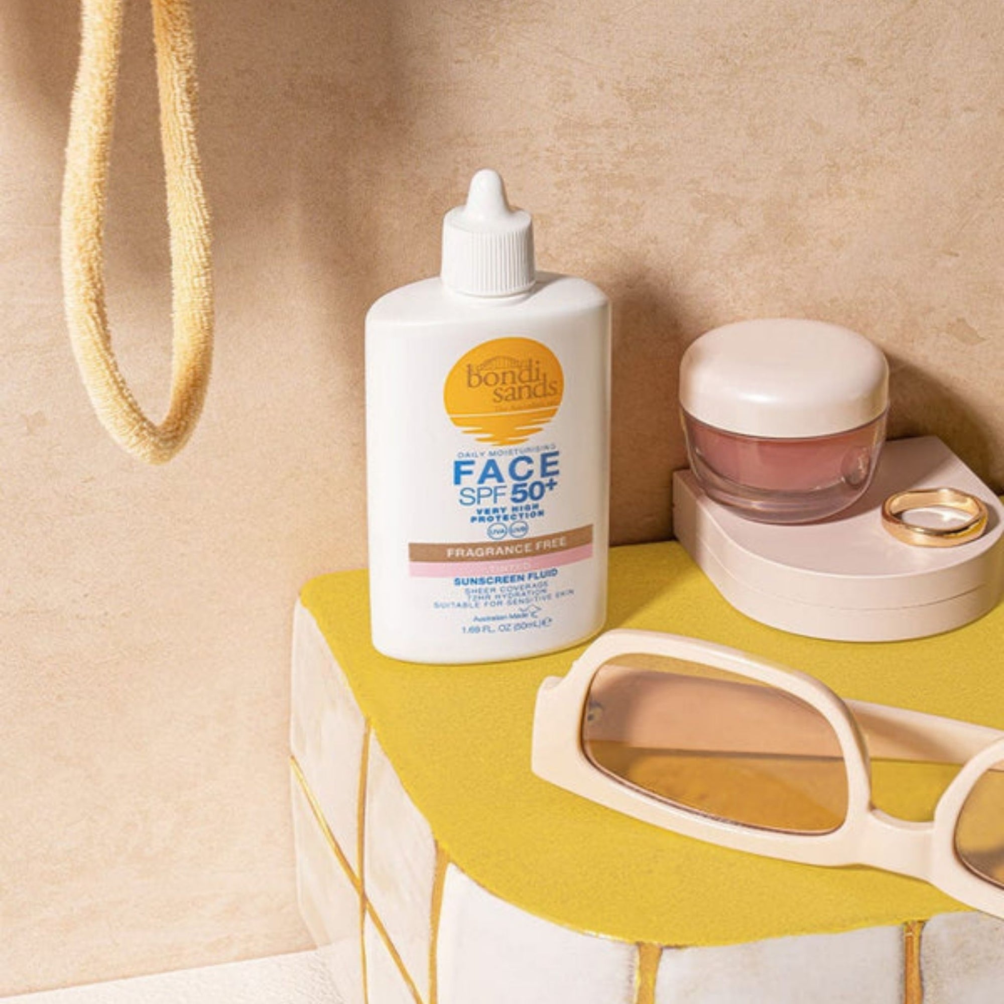 Bottle of Bondi Sands sunscreen on a yellow surface with sunglasses and a jar.
